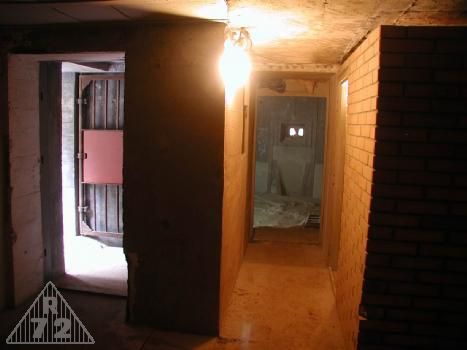 Celkový pohled na vstup do objektu, cihlovou příčku místnosti velitele a chodbičku, která spojuje pravou a levou kasematu. V horní části příčky pak ještě chybí korková tlumící vrstva.