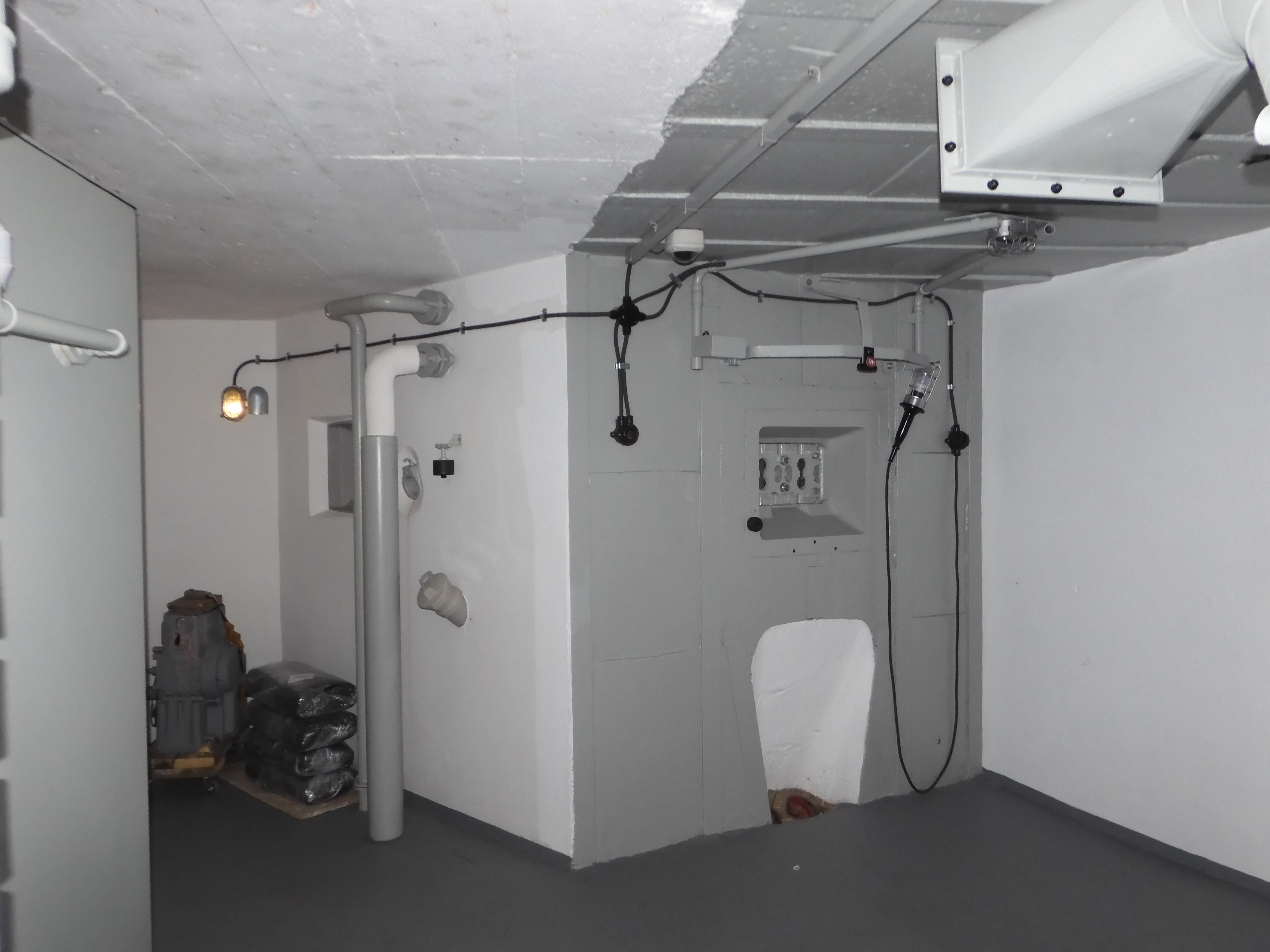 Pohled na střílnu kulometného dvojčete, rozvody elektroinstalace, montážní lampu a v levé části pak potrubí výfuku ze strojovny a odparky tamtéž.