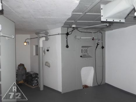 Pohled na střílnu kulometného dvojčete, rozvody elektroinstalace, montážní lampu a v levé části pak potrubí výfuku ze strojovny a odparky tamtéž.