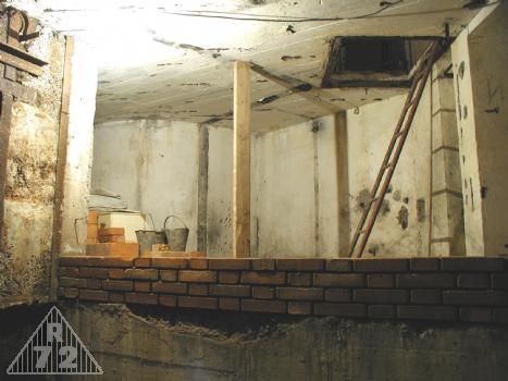 Pohled z místnosti pro zbraň G na „střední“ patro objektu. Za vznikající příčkou 30cm silnou měl být vlevo sklad munice pro G, dále soudkové WC a vpravo za žebříkem pak umývací žlab resp. v našem případě umyvadlo.<br>V horní části snímku pak průlez do horního patra.