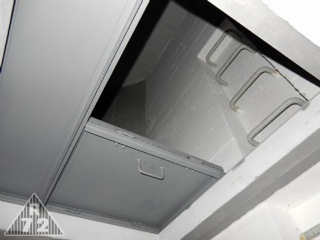 Částečně otevřený poklop průlezu mezi patry. Takto by asi průlez byl běžně otevřen. V případě potřeby se dala otevřít i druhá polovina a poklop by se pak opřel o stěnu. U objektů, kde je stěna těsně za poklopem, je ve zdi osazena klíčka, která držela poklop v otevřené poloze. K vidění je dodnes např. v objektu R-S 67. V R-S 72 instalována nebyla,neboť poklop po celkovém otevření šlo bez problémů opřít o stěnu za ním, aniž by se tento sklápěl zpět. <br>Podélná část poklopu šla samozřejmě odstranit též a otevřel se pak plný profil průlezu pro manipulaci s většími předměty.