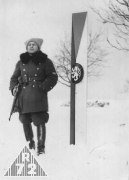Financ v krátkém zimním kožichu a papaše u hraničního znaku ČSR. 1937
