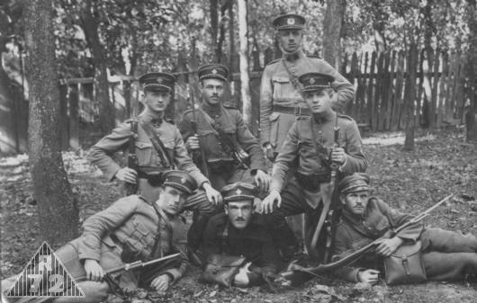 Skupina četníků ve služebních stejnokrojích z let 1921-1926. Četník stojící vzadu má na čepici ještě staré provedení znaku z roku 1921. Četník ležící uprostřed má starou rakousko-uherskou blůzu, ale již s upravenýmy nárameníky se středovým páskem.